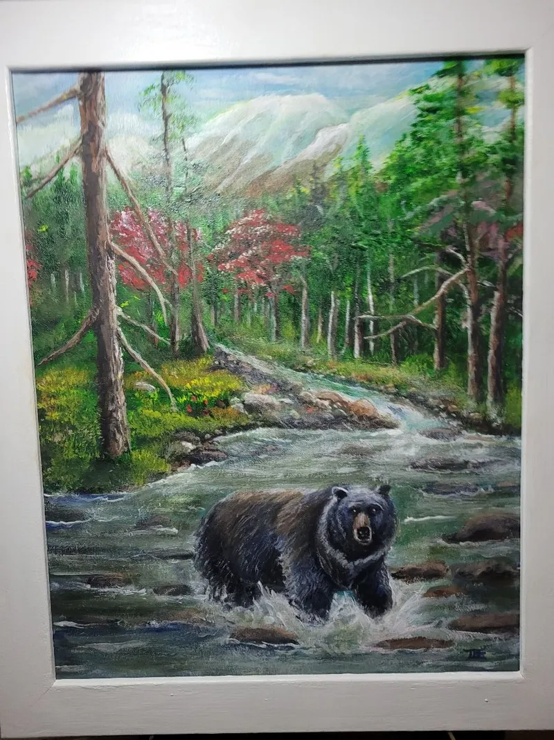 Black bear wading through a rocky mountain stream surrounded by evergreen trees and autumn foliage.