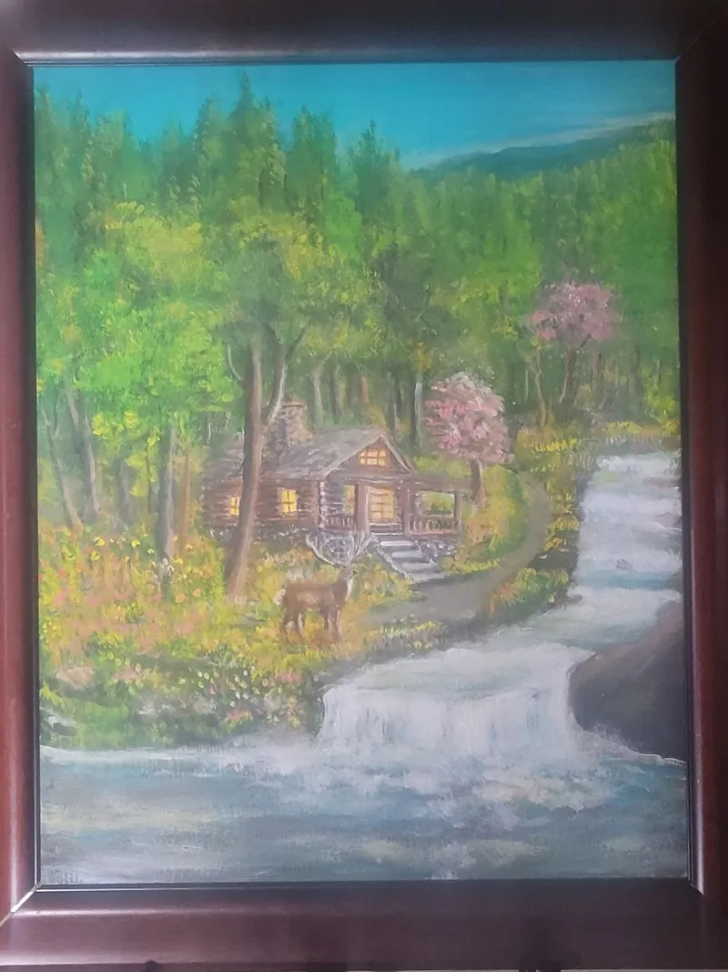 Log cabin with illuminated windows, a deer and flowering trees beside a cascading woodland waterfall.